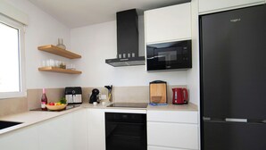 Uma cozinha moderna com armários brancos, micro-ondas preto, chaleira vermelha e lava-louças preto.