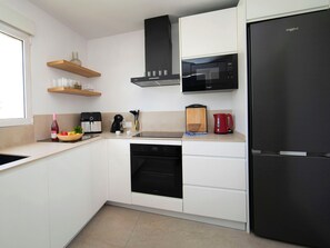 Una cocina moderna con armarios blancos, un microondas negro, un hervidor rojo y un lavavajillas negro.