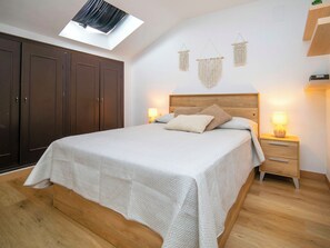 Ein Schlafzimmer mit Bett, Holzschrank, Nachttischen und einem Oberlicht.