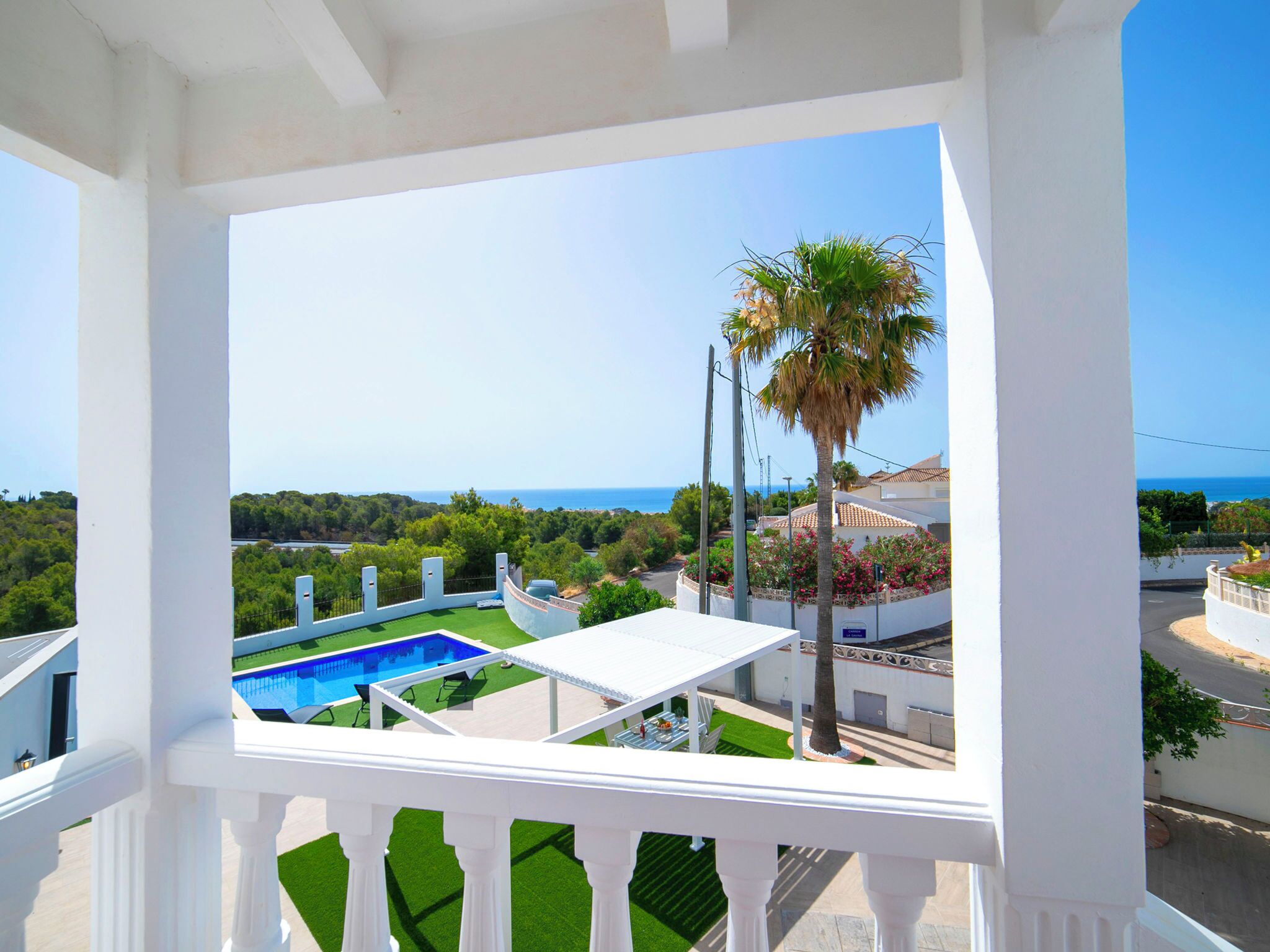 A balcony with a view of a swimming pool, a palm tree, and a coastal landscape.