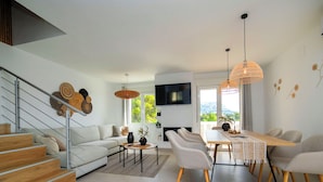 Uma sala de estar moderna com escada, área de jantar com mesa comprida e televisão na parede.