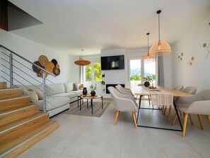 Una sala de estar moderna con una escalera, un comedor con una mesa larga y un televisor montado en la pared.