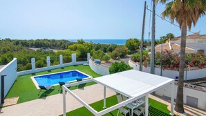 Piscina no terraço com vista para o oceano, cercada por vegetação e uma pérgula branca.