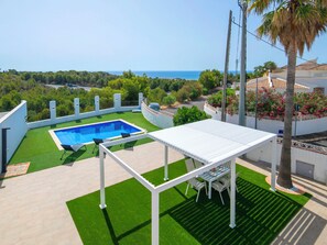 Una piscina en la azotea con vista al océano, rodeada de vegetación y una pérgola blanca.