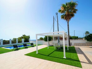 Een dakterras met zwembad, kunstgras, een pergola en een palmboom.