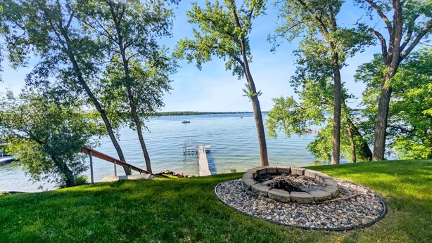 A lakeside view with a dock, a fire pit, and a grassy area. - The Cove on Lake Carlos (Carlos Township)