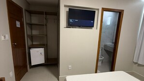 Un dormitorio con cama, televisión montada en la pared, armario y un refrigerador pequeño.