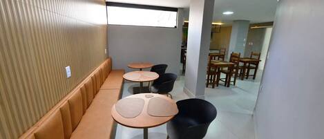 A modern interior with a long bench seating area, round tables, and chairs.