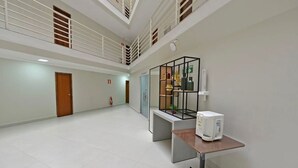 A spacious hallway with a high ceiling, a wooden door, a fire extinguisher, and a small table with a white appliance.
