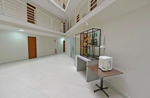 A spacious hallway with a high ceiling, a wooden door, a fire extinguisher, and a small table with a white appliance.