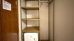 A small room with a wooden door, a white refrigerator, and a metal shelving unit with hooks.