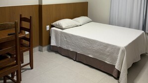 A single bed with a white bedspread, a wooden nightstand, a chair, and an air conditioning unit mounted on the wall.