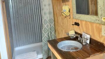 A bathroom with a wooden vanity, a mirror, a towel rack, and a shower area.