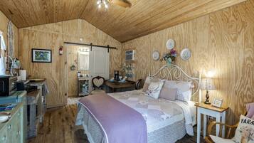 Un dormitorio acogedor con techo de madera, una cama con cabecera con forma de corazón, una mesita de noche con lámpara y una pequeña silla de madera.