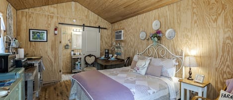 Un dormitorio acogedor con techo de madera, una cama con cabecera con forma de corazón, una mesita de noche con lámpara y una pequeña silla de madera.