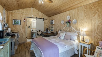 A cozy bedroom with a wooden ceiling, a bed with a heart-shaped headboard, a bedside table with a lamp, and a small wooden chair.
