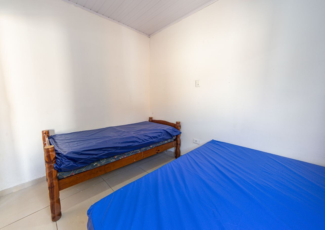 A room with two single beds, plain white walls, and a tiled floor.