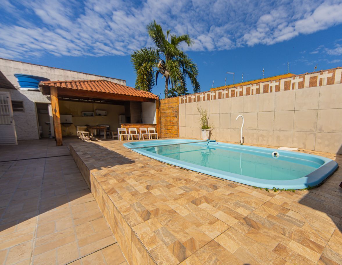 Una piscina con suelo de baldosas, zona de estar techada y una palmera al fondo.
