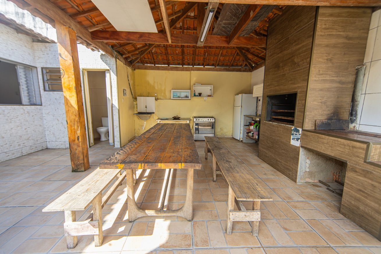 An outdoor kitchen area with a wooden table, benches, a grill, and a refrigerator.