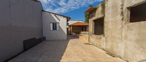 A courtyard with a tiled floor, a building with a window, and a partially constructed wall.