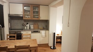 Une cuisine de taille réduite, dotée de meubles en bois, d’une table à manger, de chaises et d’un ventilateur sur pied.