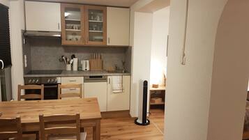 Une cuisine de taille réduite, dotée de meubles en bois, d’une table à manger, de chaises et d’un ventilateur sur pied.