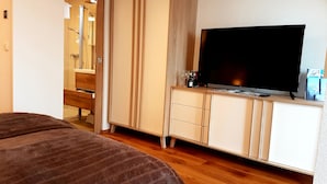 Ett sovrum med en säng, en tv placerad på ett träskåp och en duschhörna.