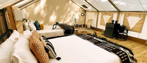 A tented accommodation with a bed, pillows, a desk, and chairs.