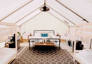 A tented accommodation with a bed, a small table, and a hanging plant.