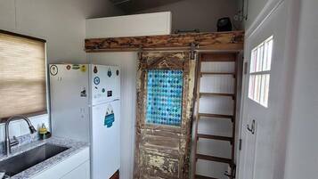 A compact kitchen with a refrigerator, sink, and wooden flooring.