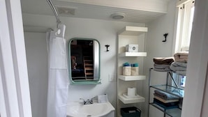 A compact bathroom with a sink, mirror, toilet, and shelves with towels. - Gorgeous Tiny House with Spectacular Countryside Vistas in Camp Wood, Texas (Camp Wood)
