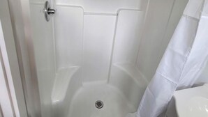A shower with a glass door, a showerhead, and a white curtain. - Gorgeous Tiny House with Spectacular Countryside Vistas in Camp Wood, Texas (Camp Wood)