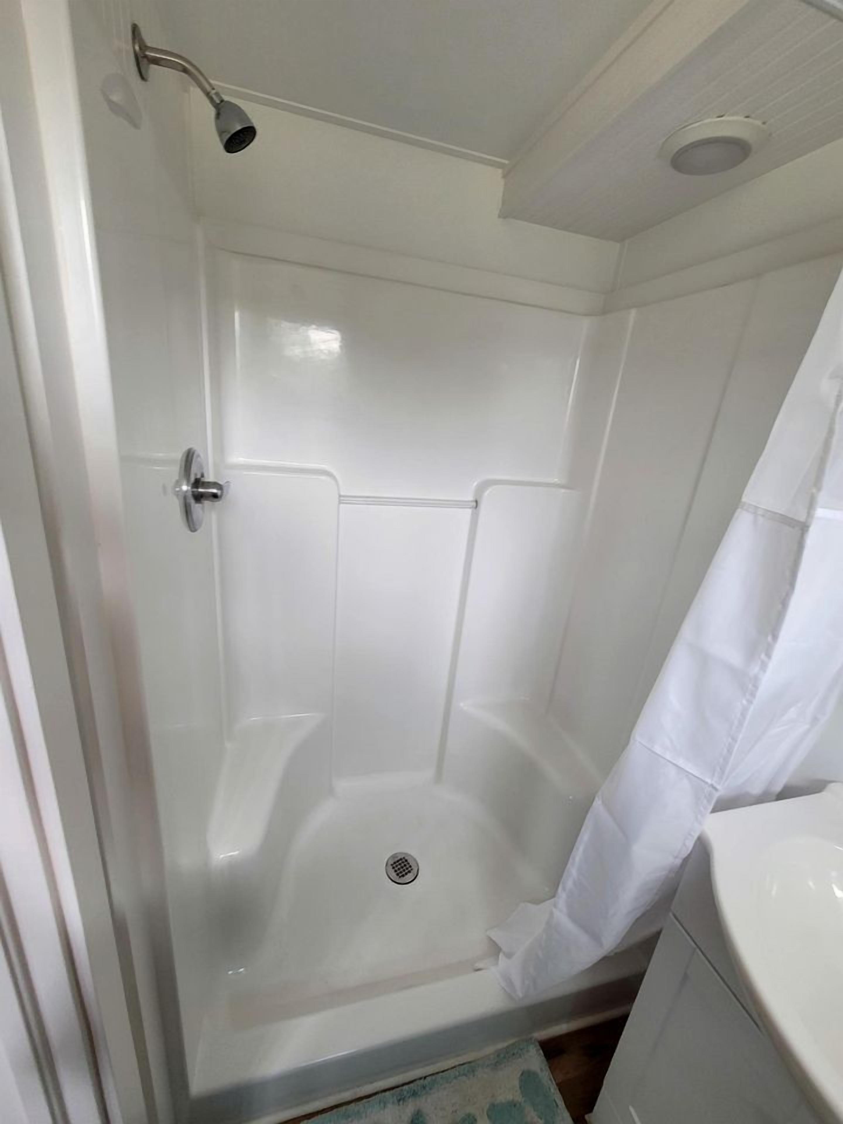 Eine Dusche mit Glastür, Brausekopf und weißem Vorhang.