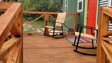 A wooden deck with a swing set and two rocking chairs.
