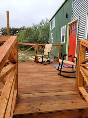 A wooden deck with a swing set and two rocking chairs.