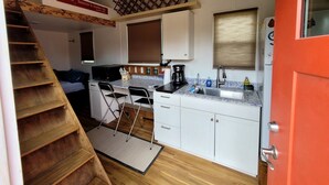 A compact kitchen with a wooden staircase, a small dining area, and a red door. - Gorgeous Tiny House with Spectacular Countryside Vistas in Camp Wood, Texas (Camp Wood)