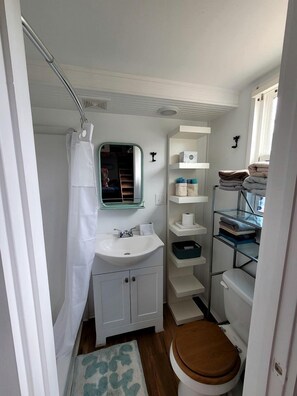Ein kleines Badezimmer mit Waschbecken, Spiegel, Toilette und Regalen mit Handtüchern.