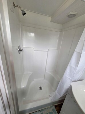 Una ducha con puerta de cristal, un rociador y una cortina blanca.