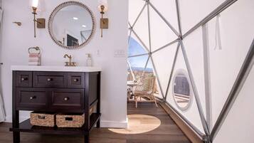 A modern bathroom with a dark wooden vanity, a round mirror, and wall-mounted lights.