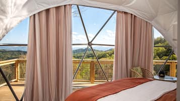 A tented accommodation with a bed, curtains, and a view of the landscape.