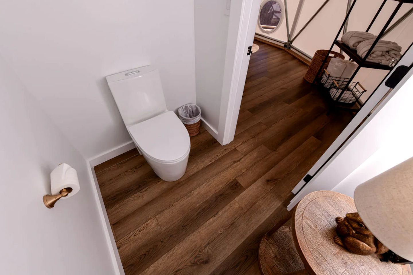 A modern bathroom with a white toilet, wooden flooring, and a small trash bin.