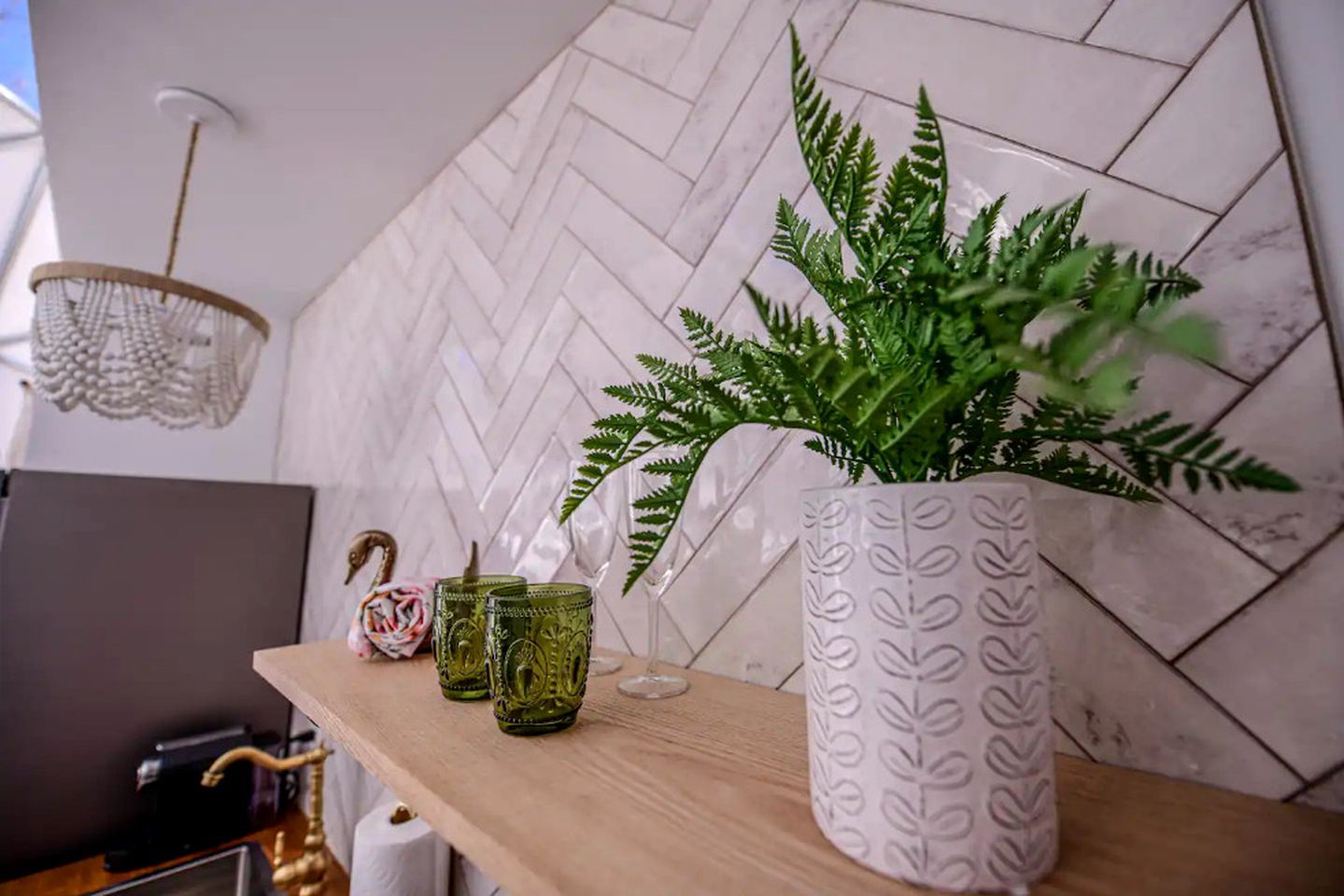 Een houten plank met een potplantvaren, twee groene glazen bekers en een decoratieve zwaan.