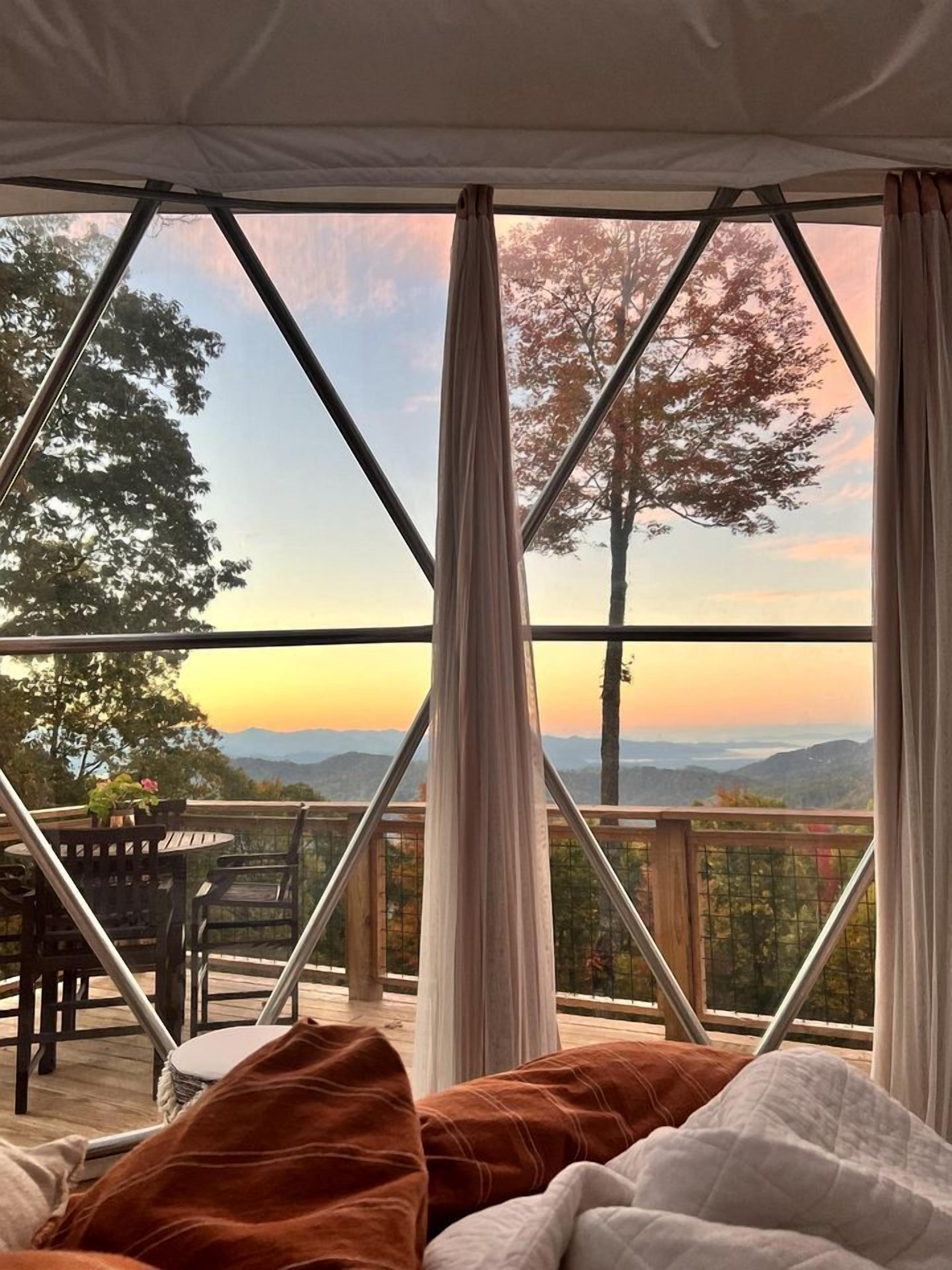A tented room with a view of a sunset over a mountainous landscape.