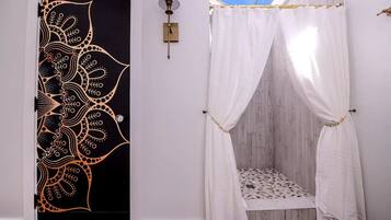 A room with a black door featuring a gold paisley pattern, a white canopy bed with a patterned bedspread, and a wall-mounted light fixture.