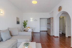 Ein Wohnzimmer mit einer Couch, einem Esstisch mit Stühlen, einer kleinen Pflanze und einer Uhr an der Wand.