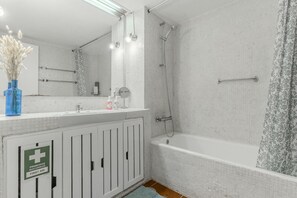 A bathroom with a shower, a sink, a mirror, and a first aid sign. - #369 One-Bedroom Apartment in Moinho (Albufeira)
