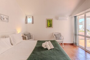 A hotel room with a bed, two chairs, a green towel, a framed picture, and a window with a view. - #369 One-Bedroom Apartment in Moinho (Albufeira)
