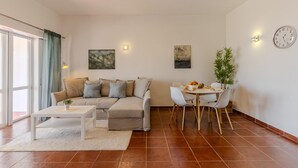 Una sala de estar con sofá, mesa de centro, mesa de comedor, sillas y un reloj en la pared.