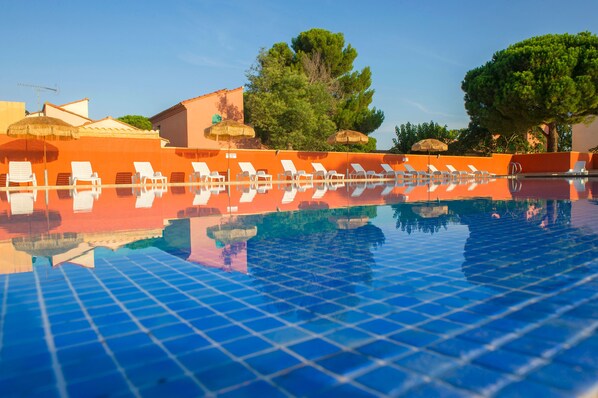 A swimming pool with lounge chairs and umbrellas, surrounded by trees and buildings.