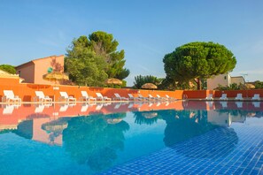 A swimming pool with clear blue water, surrounded by white lounge chairs and orange walls.